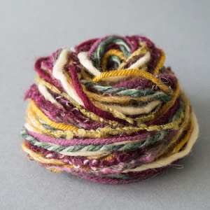 May include: A ball of yarn with a mix of burgundy, cream, gold, and green threads.