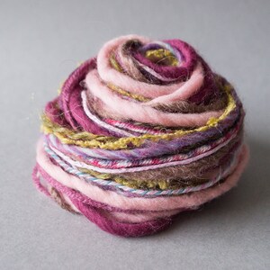 May include: A ball of yarn with pink, purple, brown, and green threads. The yarn is wound into a tight ball.