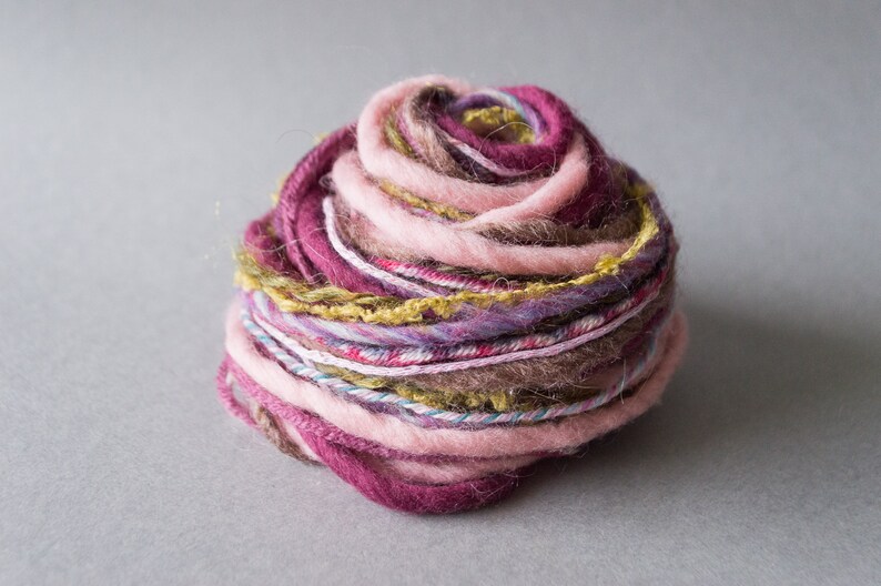 May include: A ball of yarn with pink, purple, brown, and green threads. The yarn is wound into a tight ball.
