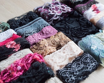 May include: A collection of various lace trims in a variety of colors, including black, white, pink, and blue. The lace features floral and geometric patterns, with some having beaded accents. The trims are arranged in neat rows, showcasing their textures.