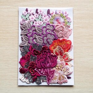 May include: A selection of embroidered floral appliques in shades of pink, purple, red, and orange. The appliques are displayed on a white rectangular card, featuring intricate floral patterns.