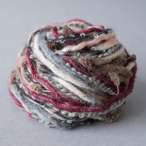 Puede incluir: Un ovillo de lana con una variedad de colores y texturas, incluyendo rosa, blanco, gris, marrón y rojo. La lana tiene una textura peluda y está hecha de múltiples hebras.