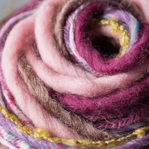 May include: Close-up of a ball of yarn with pink, purple, brown, and yellow threads. The yarn is wound in a spiral pattern.
