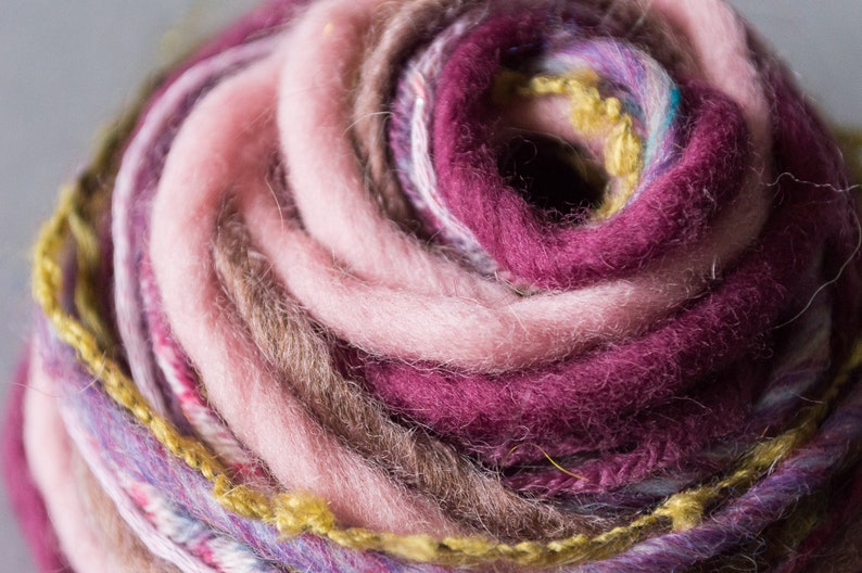 May include: Close-up of a ball of yarn with pink, purple, brown, and yellow threads. The yarn is wound in a spiral pattern.