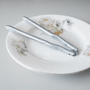 May include: Two silver nutcrackers on a white plate with a floral design. The nutcrackers are made of metal and have a textured surface.