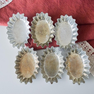 Può includere: Sei stampi per crostate in metallo color argento con bordi ondulati. Gli stampi sono disposti in due file da tre su una superficie bianca.