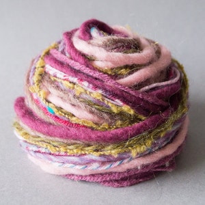 Può includere: Un gomitolo di lana di diversi colori, tra cui rosa, viola, marrone e verde. La lana è composta da una varietà di fibre, tra cui lana e cotone.