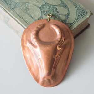 May include: A vintage copper mould shaped like a bull's head with horns. The mould has a hanging loop and is used for making desserts.