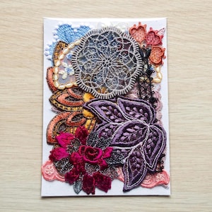 May include: A selection of colourful embroidered lace appliques on a white card. The appliques feature a large, intricate silver doily, a deep purple floral design, and other floral and abstract shapes in shades of orange, pink, and blue.