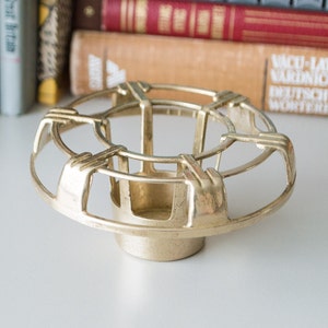 May include: A gold metal flower frog with a circular design. The frog has a round base and a raised, open top.