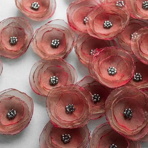 Può includere: Una collezione di delicati fiori di tessuto a strati in tonalità rosa e rosse. Ogni fiore presenta un gruppo di perline d'argento al centro. Questi abbellimenti floreali fatti a mano sono ideali per l'artigianato e aggiungono un tocco di eleganza a vari progetti.
