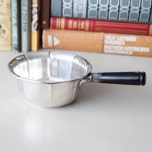 May include: A silver serving dish with a black plastic handle. The dish has a fluted rim and a rounded bottom.