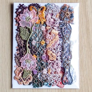 Könnte beinhalten: Eine Sammlung farbenfroher, aufwendig gestalteter Spitzenapplikationen in verschiedenen floralen und abstrakten Mustern. Die Applikationen weisen Farbtöne von Rosa, Grün, Orange und Lila auf, mit detaillierten Nähten und Texturen. Die Spitze ist auf weißem Hintergrund angeordnet.