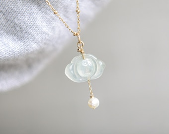 May include: A delicate gold necklace featuring a cloud-shaped pendant carved from a pale green gemstone. A small, round pearl dangles below the cloud. The necklace is displayed against a soft gray background.