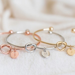A handcrafted knot bracelet with an elegant design, featuring a personalized initial charm. The knot and unique charm add a personalized touch, making it a perfect accessory for any outfit. Ideal for adding a subtle yet distinctive statement.