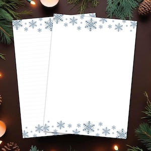 May include: Two white sheets of stationery with a snowflake border in shades of blue. One sheet is lined, the other is blank. The stationery is surrounded by pine needles, pine cones, and lit candles, creating a festive winter theme.