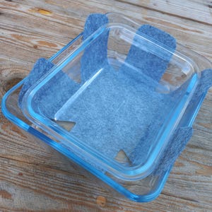 Può includere: Due teglie da forno in vetro con cuscinetti in feltro blu sui bordi. I cuscinetti sono progettati per proteggere le superfici dal calore.