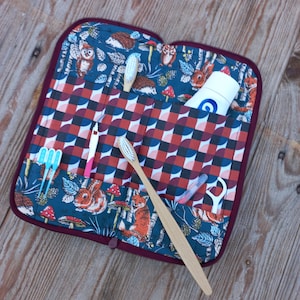 May include: A burgundy zippered travel case with a blue and green patterned fabric interior. The case is open and contains a variety of items, including toothbrushes, floss, and a tube of toothpaste.