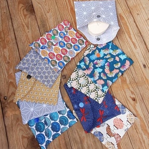 Può includere: Assortimento di bustine in tessuto con vari motivi, tra cui disegni geometrici, floreali e astratti. Le bustine sono in cotone e hanno una chiusura a bottone.