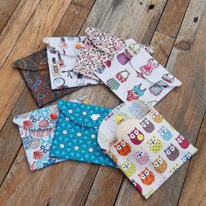 Puede incluir: Una colección de bolsas de tela con varios diseños, incluyendo florales, geométricos y de búhos. Cada bolsa está doblada y asegurada con un cierre de botón. Las bolsas están dispuestas sobre una superficie de madera.