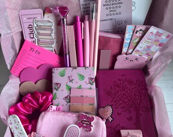 May include: A pink gift box filled with stationery and accessories. Items include pens, pencils, a notebook, stickers, a hair clip, and a nail file. The box contains a book review sheet and a sticker that says "BOOKS".