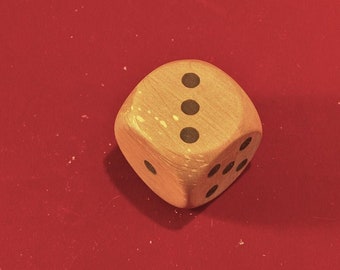 May include: A wooden dice with black dots on each side. The dice is showing the number three.