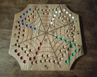May include: A wooden spider web game board with red, blue, green, and white playing pieces. The board has a spider web design with the letters T, C, K, and O in the center.