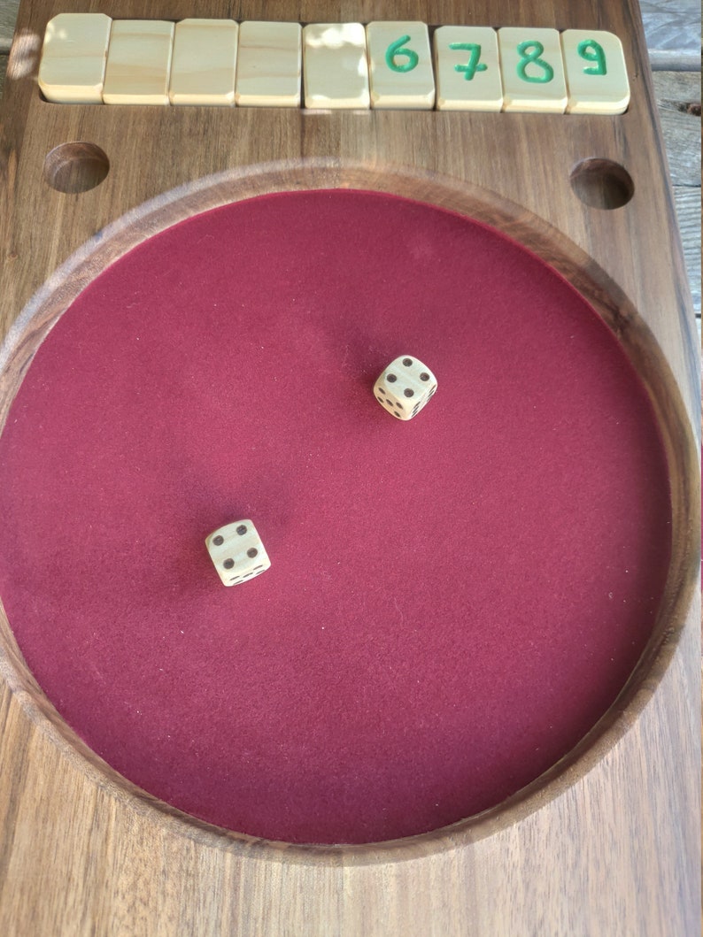 May include: A wooden game board with a red felt playing surface. Two dice have been rolled onto the felt surface. The numbers 6, 7, 8, and 9 are written on the board.