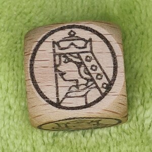 May include: A wooden cube with a circular design of a person wearing a crown and a robe. The design is in black and white.