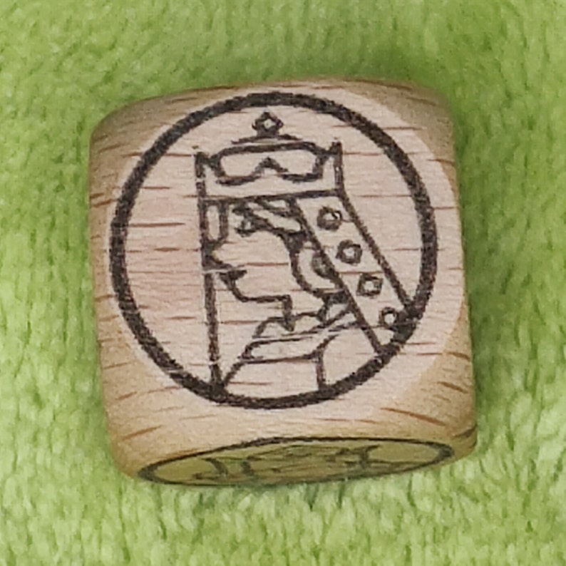 May include: A wooden cube with a circular design of a person wearing a crown and a robe. The design is in black and white.