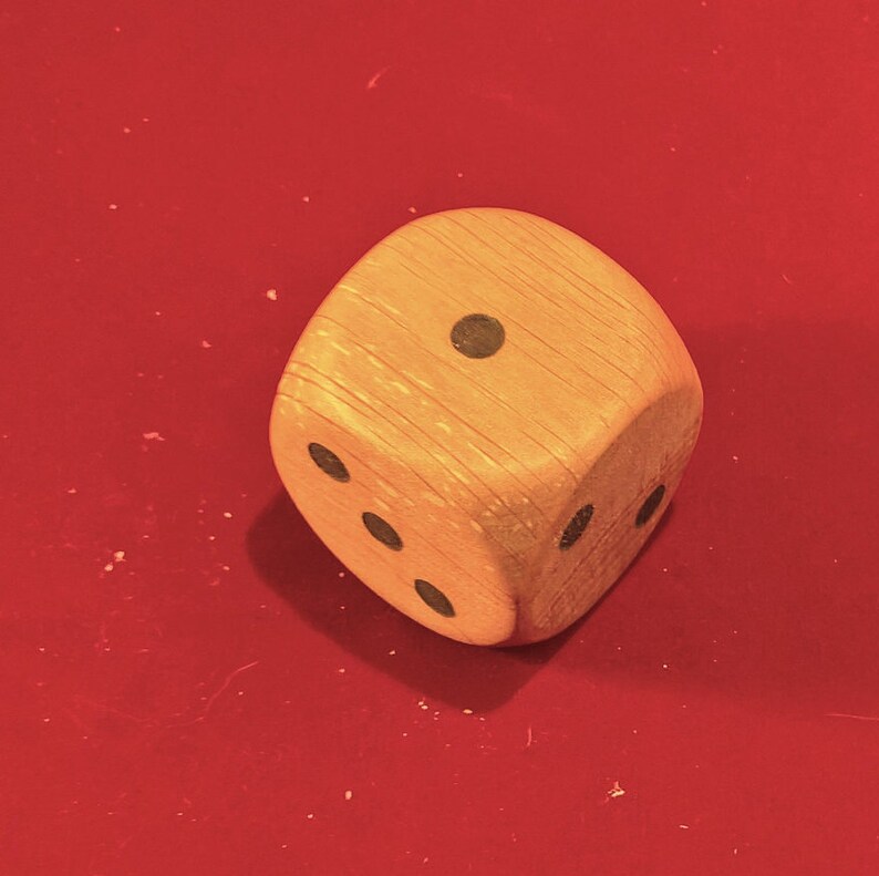 Op de afbeelding: Een houten dobbelsteen met zwarte stippen op elke zijde. De dobbelsteen toont het nummer &eacute;&eacute;n.