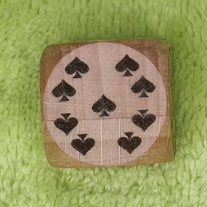 May include: A wooden block with a circular design featuring nine black spade symbols.