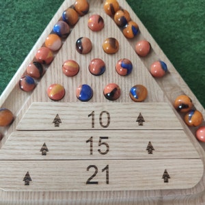 May include: A wooden triangular game board with a scoring area at the bottom. The board has three rows of numbers: 10, 15, and 21. The board is filled with marbles of various colors, including orange, blue, and brown.