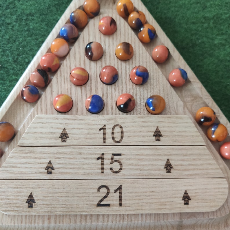May include: A wooden triangular game board with a scoring area at the bottom. The board has three rows of numbers: 10, 15, and 21. The board is filled with marbles of various colors, including orange, blue, and brown.