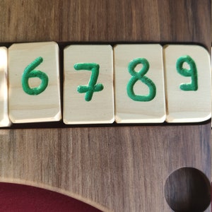 May include: Close-up of a wooden board with four wooden tiles, each with a green number painted on it. The numbers are 6, 7, 8, and 9.