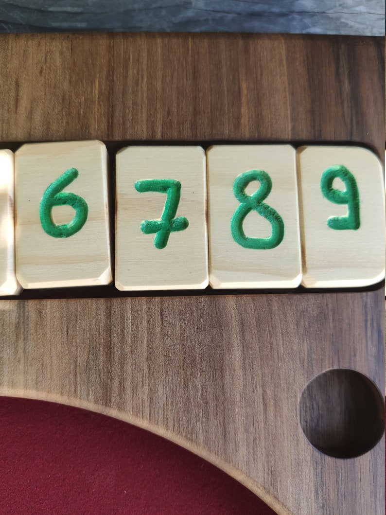 May include: Close-up of a wooden board with four wooden tiles, each with a green number painted on it. The numbers are 6, 7, 8, and 9.