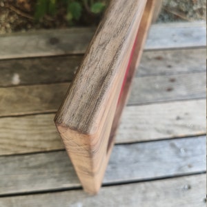 May include: Close-up of the corner of a wooden frame with a red velvet lining. The frame is made of dark wood with a natural grain.