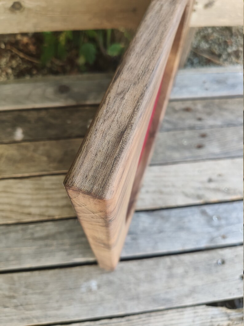 May include: Close-up of the corner of a wooden frame with a red velvet lining. The frame is made of dark wood with a natural grain.