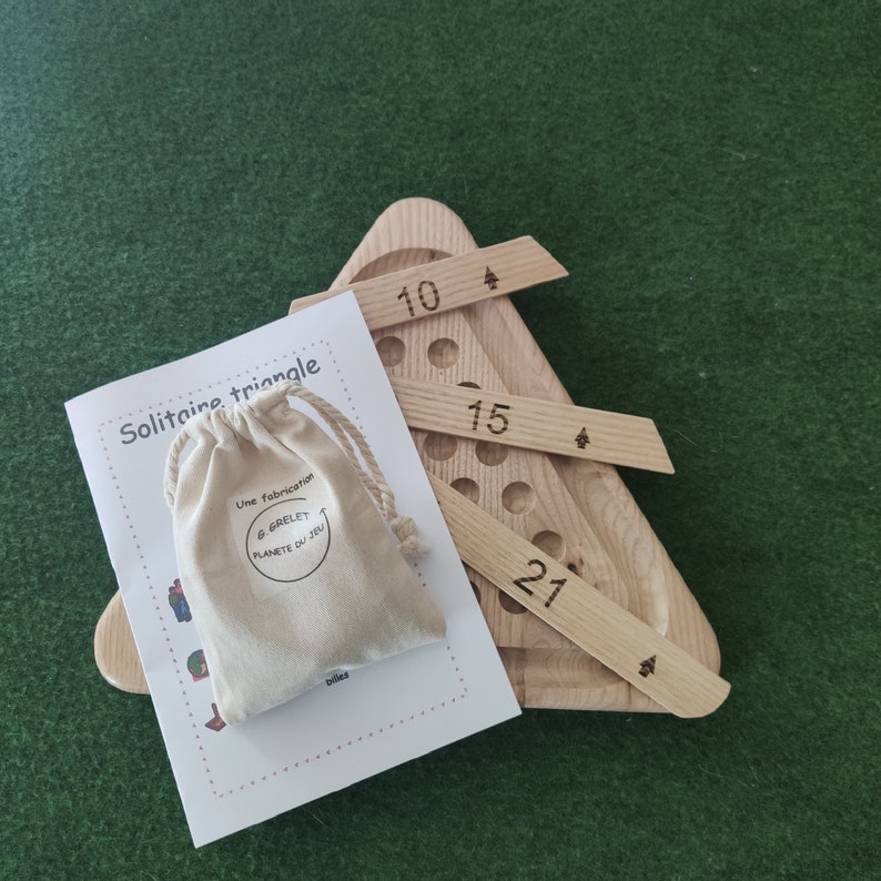 May include: A wooden triangle game with a bag of game pieces. The game board has numbers 10, 15, and 27 printed on it. The game is called "Solitaire Triangle" and is made by "G. Grelet Planete du Jeu".
