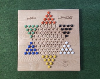 May include: A wooden game board with a star-shaped playing area. The board has five points, each with a different color of marbles: green, blue, yellow, white, and orange. The board is labeled "DAMES" and "CHINOISES".