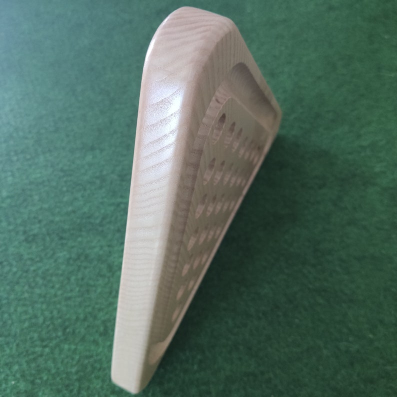 May include: A wooden triangular game board with a series of holes drilled into the surface. The board is made of light wood and has a smooth finish.