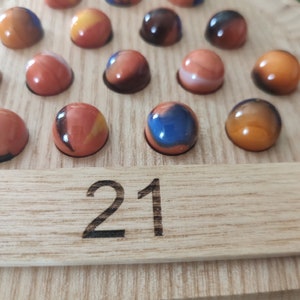 May include: A wooden game board with 21 marbles in various colors, including orange, blue, and black. The board has a number "21" printed on it.