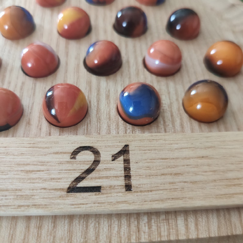 May include: A wooden game board with 21 marbles in various colors, including orange, blue, and black. The board has a number "21" printed on it.