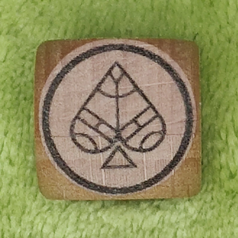 May include: A wooden block with a black circle around a spade playing card symbol. The spade is stylized with a geometric design.