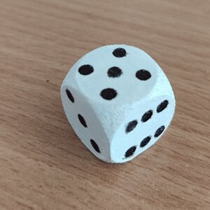 Op de afbeelding: Een witte houten dobbelsteen met zwarte stippen op elke zijde. De dobbelsteen toont het getal vijf.
