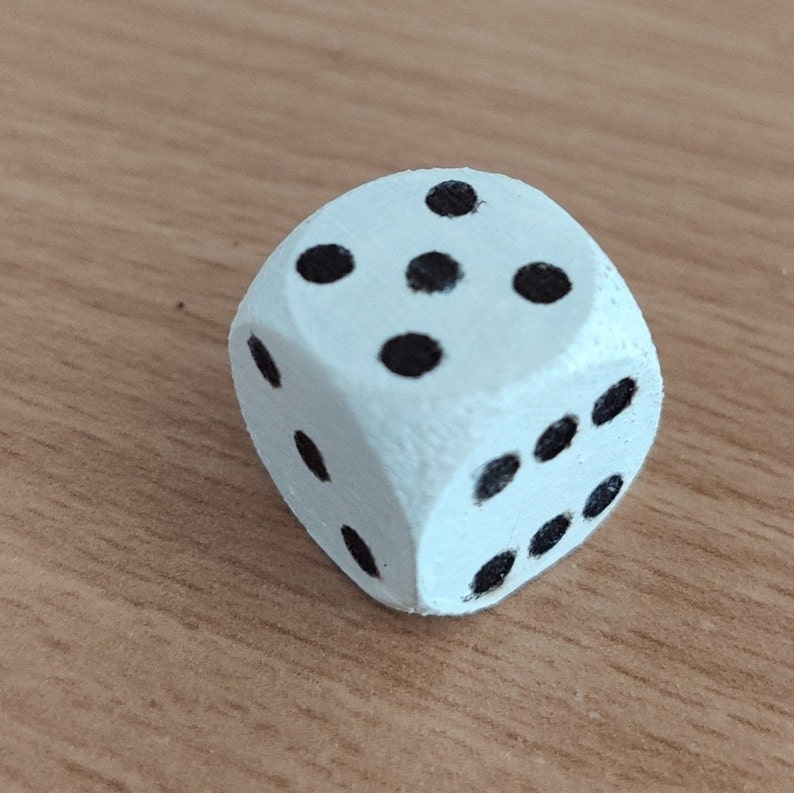 Op de afbeelding: Een witte houten dobbelsteen met zwarte stippen op elke zijde. De dobbelsteen toont het getal vijf.
