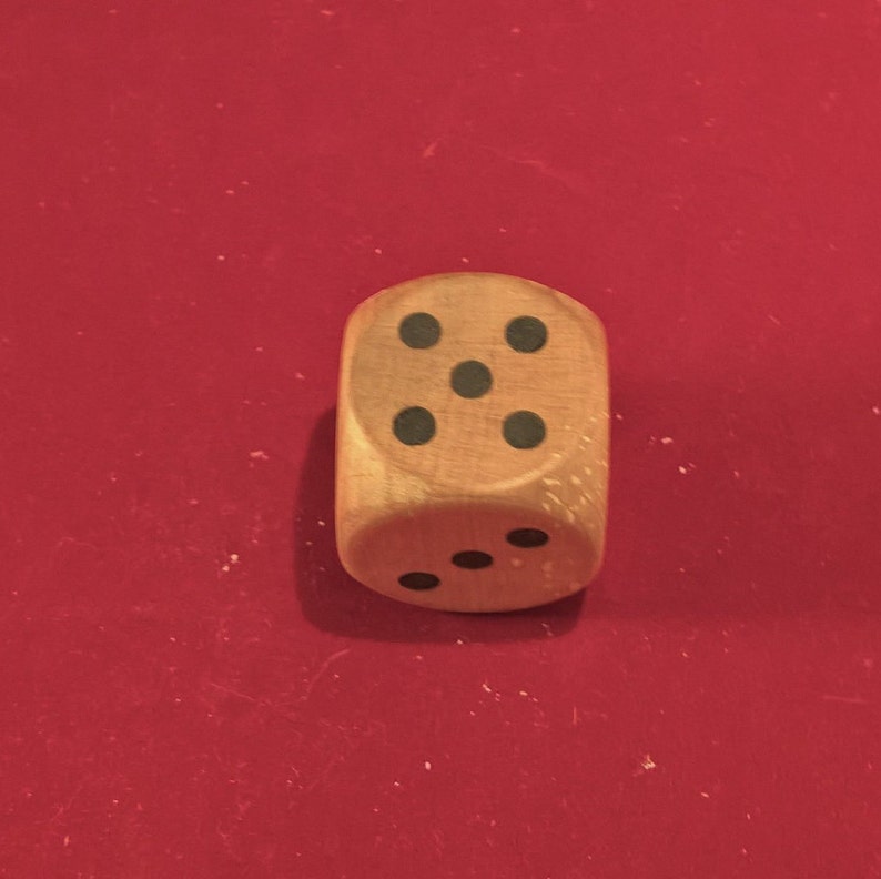 Op de afbeelding: Een houten dobbelsteen met zwarte stippen op elke zijde. De dobbelsteen toont het getal vijf.