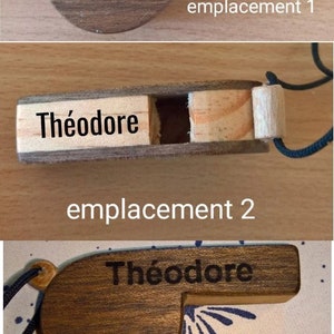 K&ouml;nnte beinhalten: Eine Holzpfeife mit dem eingravierten Namen Th&eacute;odore auf der Oberfl&auml;che. Die Pfeife wird in drei verschiedenen Positionen gezeigt, die als emplacement 1, emplacement 2 und emplacement 3 beschriftet sind, mit einer schwarzen Kordel zum Aufh&auml;ngen.