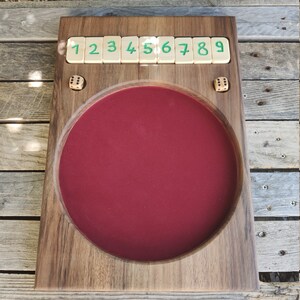 May include: A wooden game board with a red felt centre and a row of numbered tiles from 1 to 9. Two dice are on the board.