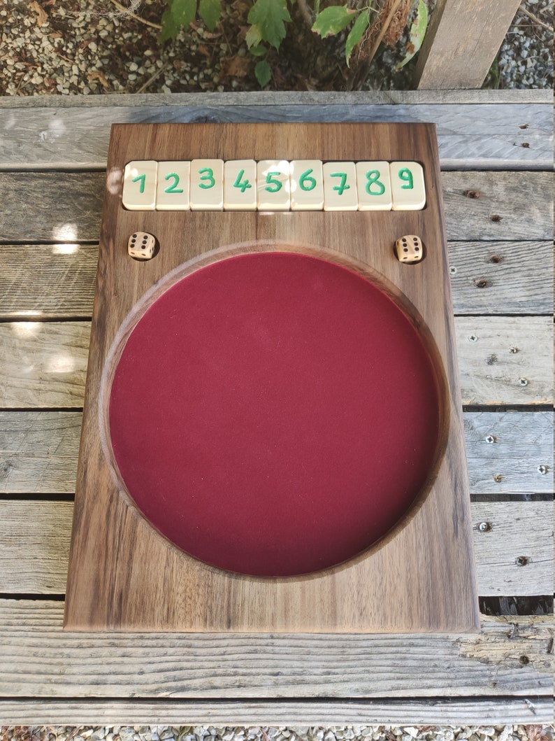 May include: A wooden game board with a red felt centre and a row of numbered tiles from 1 to 9. Two dice are on the board.